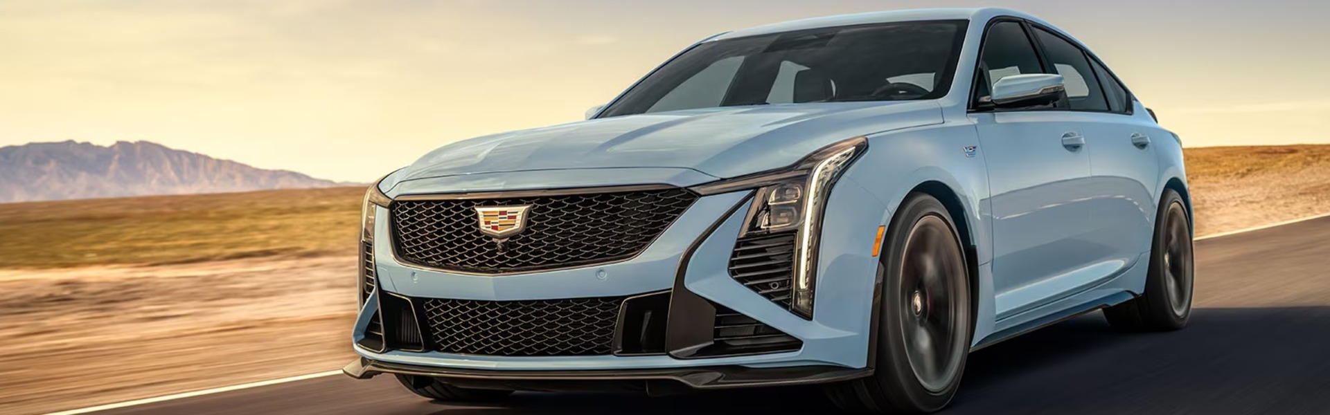 2025 Cadillac CT5-V performance sedan driving on an open desert road, featuring a light blue exterior.