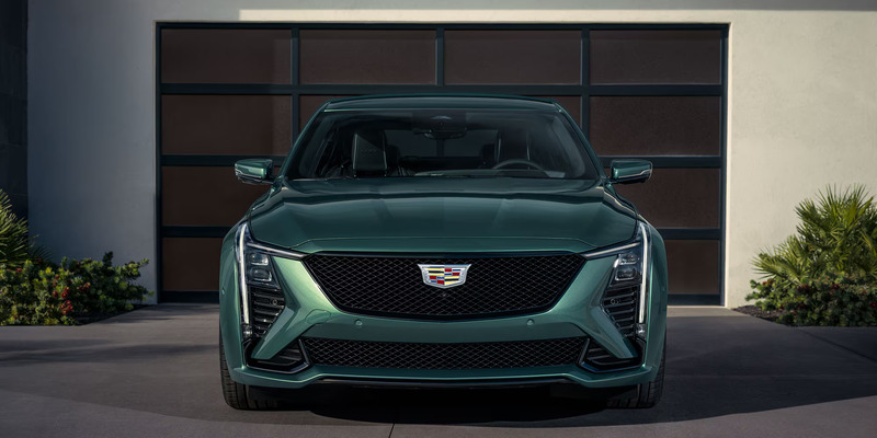 Front view of a sleek, green Cadillac CT5-V parked in a driveway. The car's bold design features angular headlights and a prominent grille, exuding a modern luxury vibe.