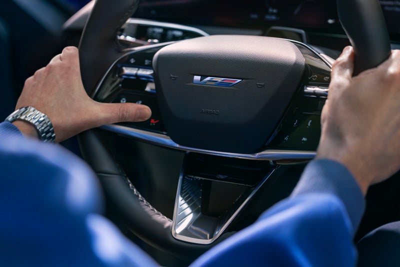 Close-up of a Man About to Press the V-Button on the 2026 OPTIQ-V Steering Wheel | AutoNation Cadillac West Amarillo in AMARILLO TX