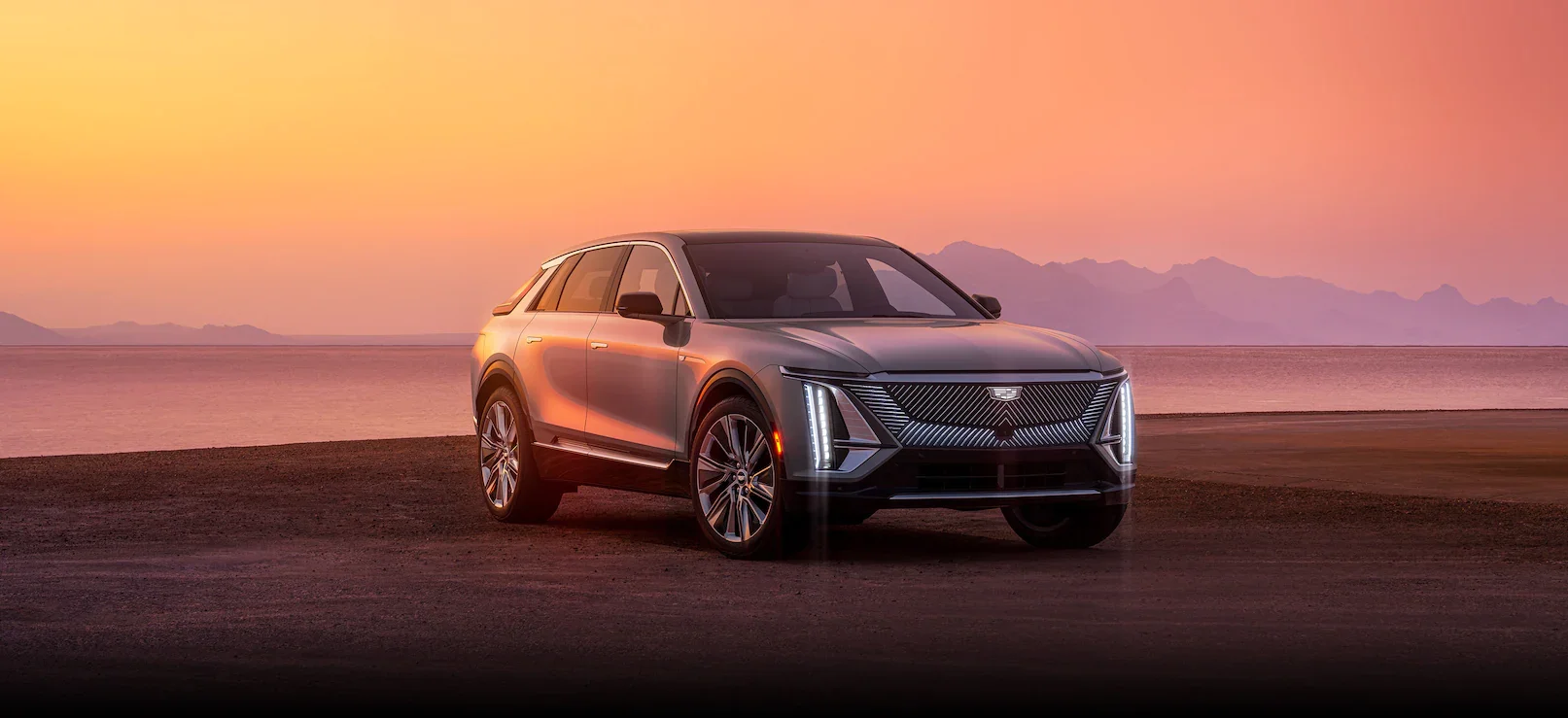 Silver Cadillac SUV driving at sunset.