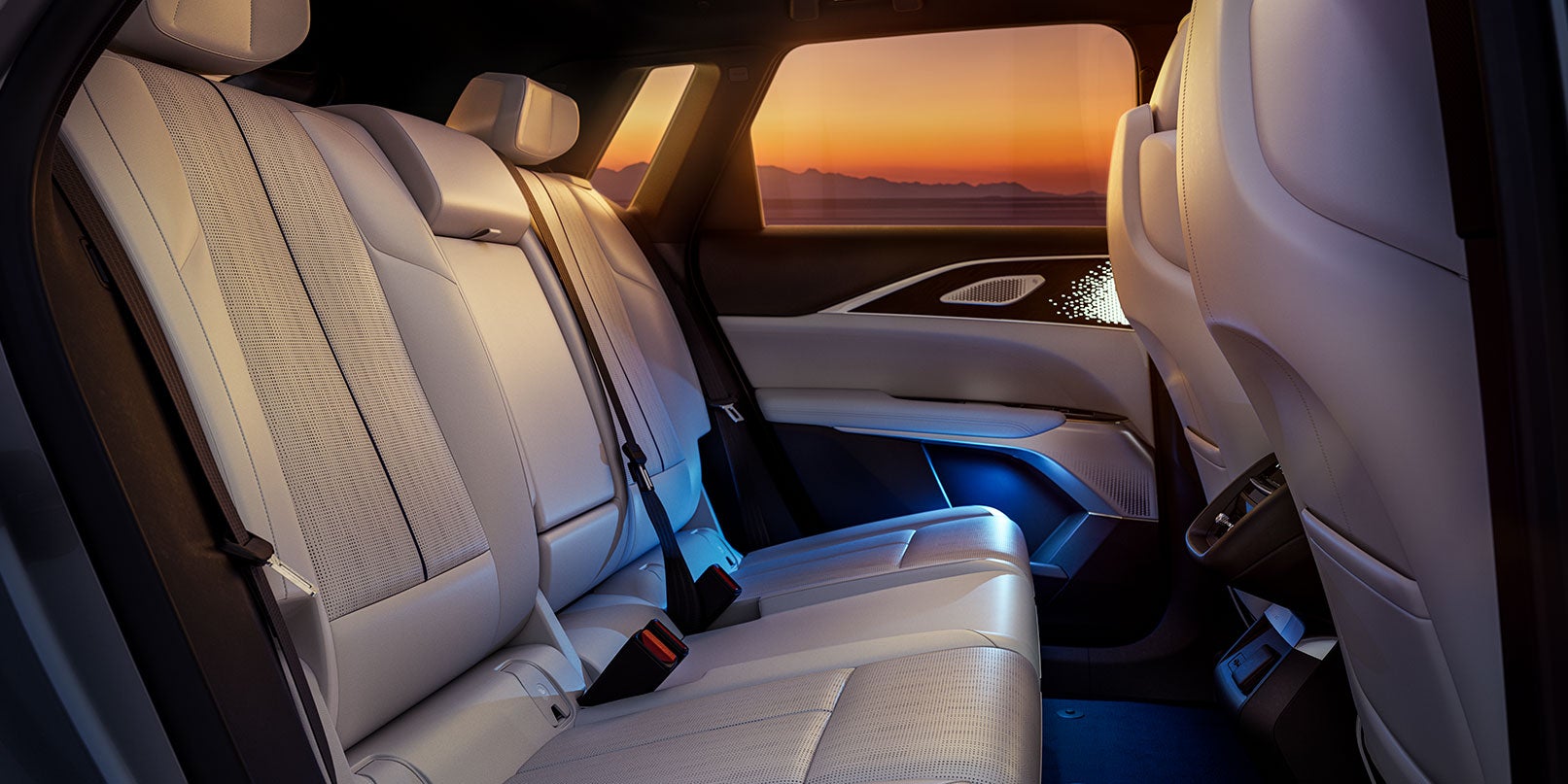 Rear seats of a car with light-colored upholstery and ambient lighting during sunset.
