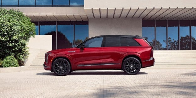 A red 2027 Cadillac VISTIQ with black wheels parked in a scenic outdoor setting.